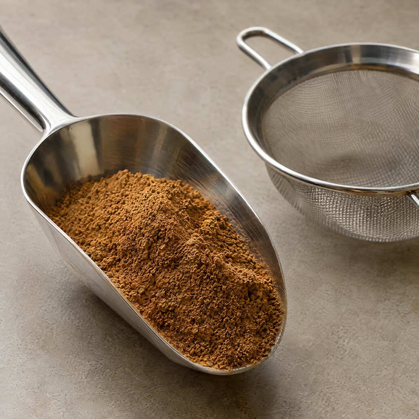 Steel scoop of fine tobacco dust beside a stainless steel sieve