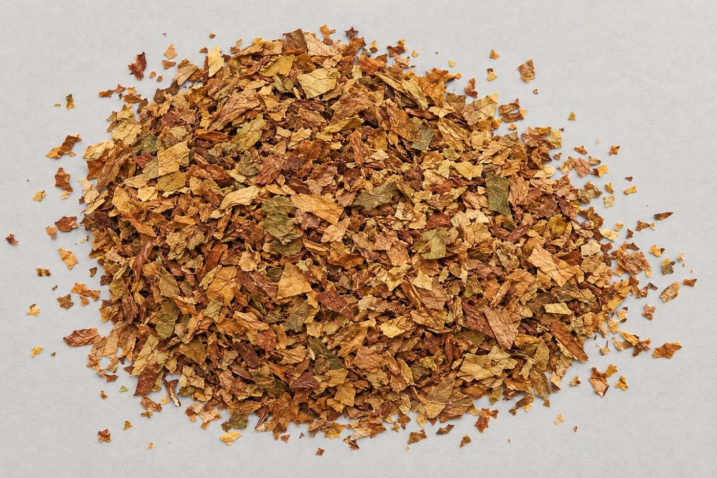 Top-down view of a heap of golden-brown cut tobacco lamina flakes on a grey board