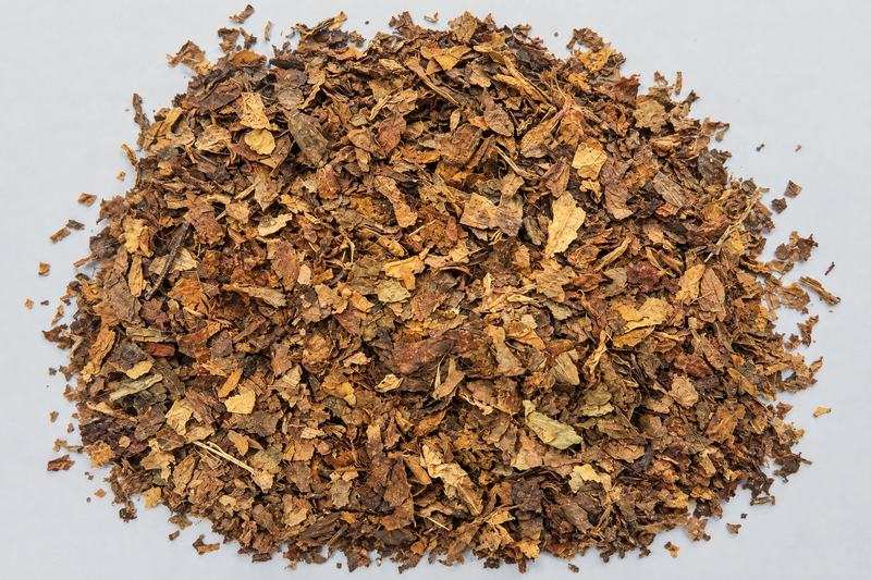 Top-down view of a heap of dark-brown coarse tobacco scrap on a light board